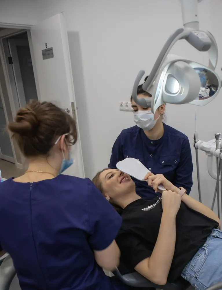 Пациентка с брекетами улыбается, глядя в зеркало после приёма